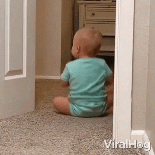 A Baby Is Sitting On The Floor In A Room Looking Out Of A Doorway . GIF