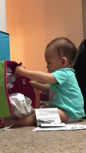 A Baby Is Sitting On The Floor Playing With A Box That Says " For Your Safety " On It GIF