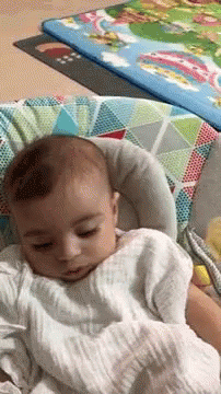 A Baby Is Sleeping In A Bouncer With A Blanket On It . GIF