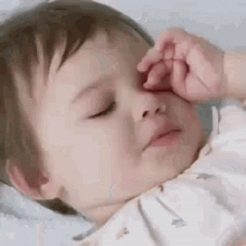 A Baby Is Sleeping With His Eyes Closed And Rubbing His Nose . GIF