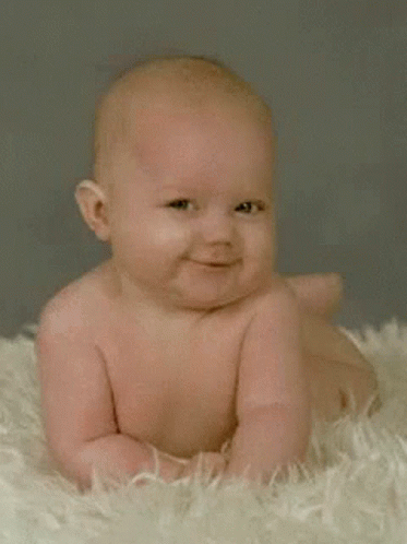 A Baby Is Smiling While Laying On A Fluffy Blanket GIF