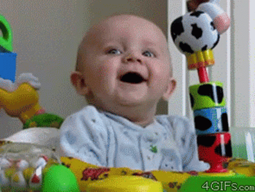 A Baby Is Smiling While Sitting In A Crib With Toys And The Website 4Gifs.com Is Visible In The Corner GIF