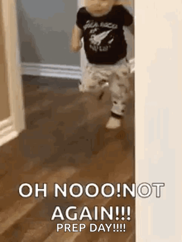A Baby Is Standing On A Wooden Floor In Front Of A Door . GIF