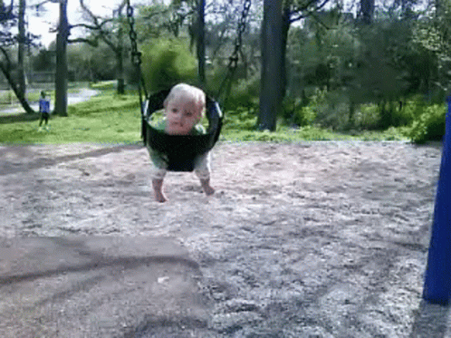 A Baby Is Swinging On A Swing Set In The Dirt GIF