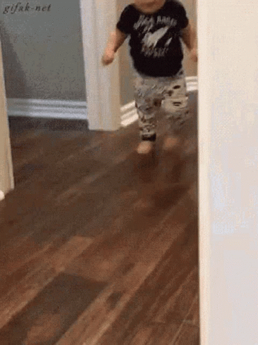 a baby is walking on a wooden floor wearing a black shirt that says rock n roll