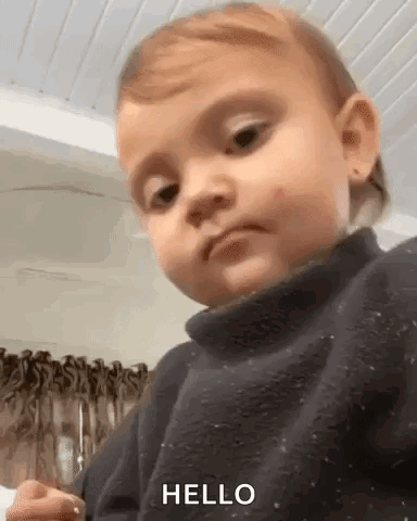 A Baby Is Wearing A Black Sweater And Making A Funny Face . GIF