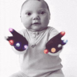 a baby is wearing a white shirt and black gloves with colored dots on them