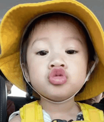 A Baby Is Wearing A Yellow Hat And Making A Funny Face With His Lips . GIF