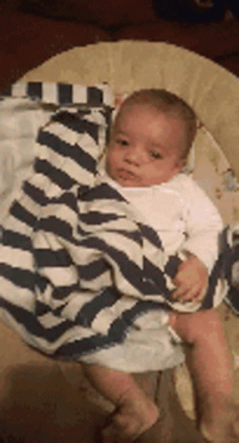 A Baby Is Wrapped In A Striped Blanket And Sitting In A Bouncer . GIF
