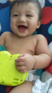 A Baby Laying On A Blanket With A Yellow Toy GIF