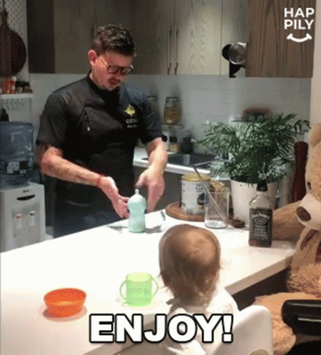 A Baby Sitting At A Table With A Bottle Of Jack Daniel 'S In The Background GIF