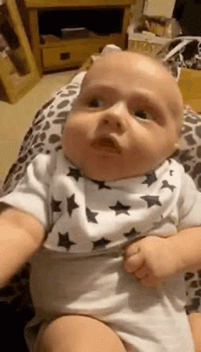 A Baby Wearing A Bib Is Being Held By A Person And Making A Funny Face . GIF