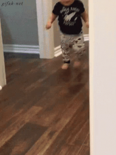 A Baby Wearing A Black Shirt That Says Rock N Roll Is Running On A Wood Floor GIF