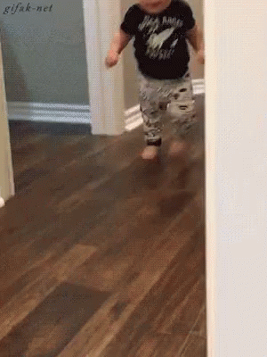 A Baby Wearing A Black Shirt That Says Rock N Roll Is Running On A Wooden Floor . GIF