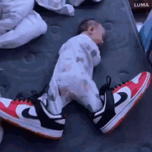 A Baby Wearing A Pair Of Nike Shoes Is Sleeping On A Bed . GIF