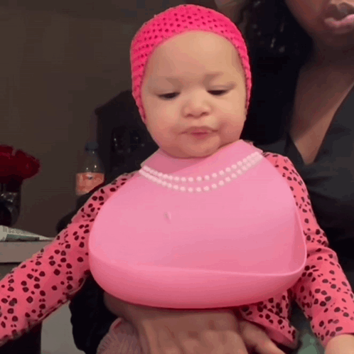 a baby wearing a pink bib and a pink headband is being held by a woman
