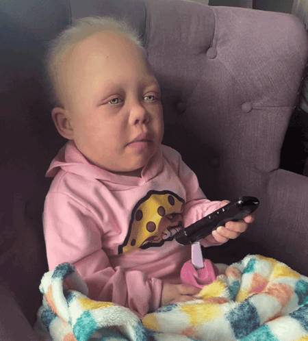 A Baby Wearing A Pink Shirt With Cheese On It Holds A Remote Control GIF