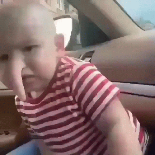 A Baby Wearing A Red And White Striped Shirt Is Sitting In The Back Seat Of A Car GIF