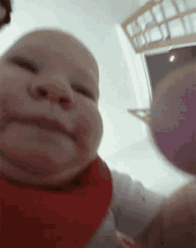 A Baby Wearing A Red Bib Is Looking At The Camera And Smiling . GIF
