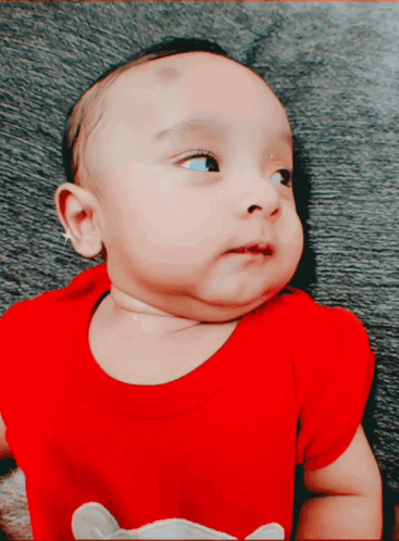 A Baby Wearing A Red Shirt With A Mouse On It Looks At The Camera GIF