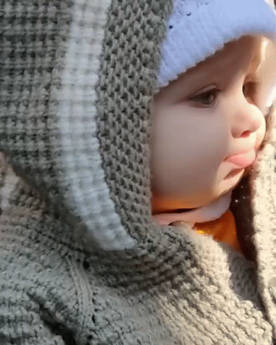 A Baby Wearing A Sweater With A Hood And A White Hat GIF