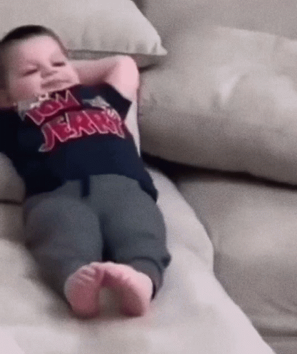A Baby Wearing A Tom Jerry Shirt Laying On A Couch GIF