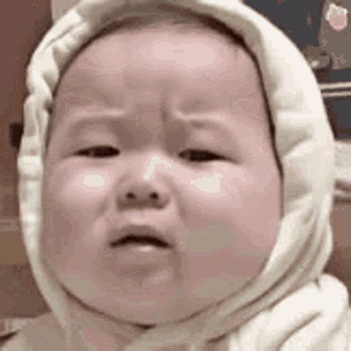 A Baby Wearing A White Hooded Sweater Is Crying . GIF