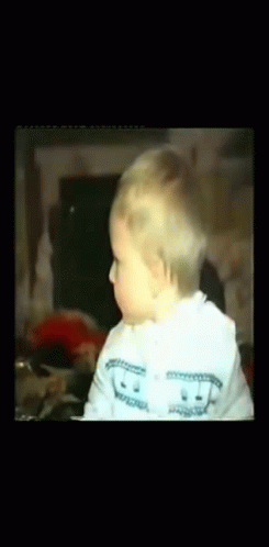 A Baby Wearing A White Sweater With A Smiley Face On It GIF