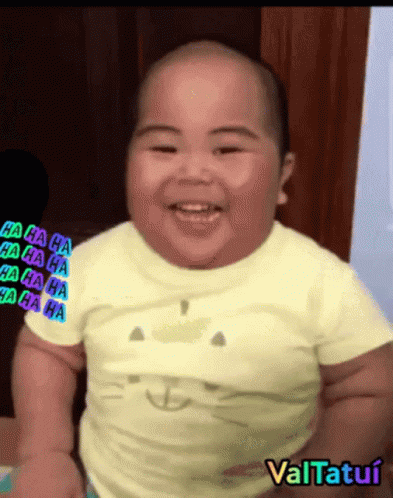 A Baby Wearing A Yellow Shirt With A Cat On It Smiles GIF
