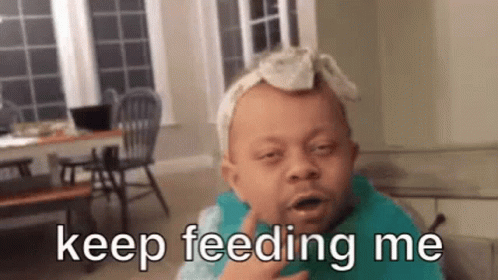 A Baby With A Bandana On His Head Is Wearing A Bib And Saying Keep Feeding Me . GIF