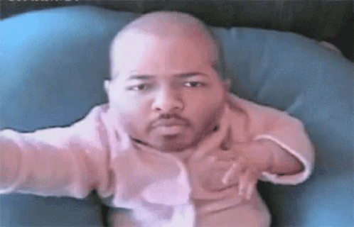 A Baby With A Beard Is Sitting On A Blue Pillow Looking At The Camera . GIF