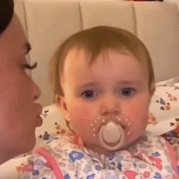 a baby with a pacifier in its mouth is looking at the camera