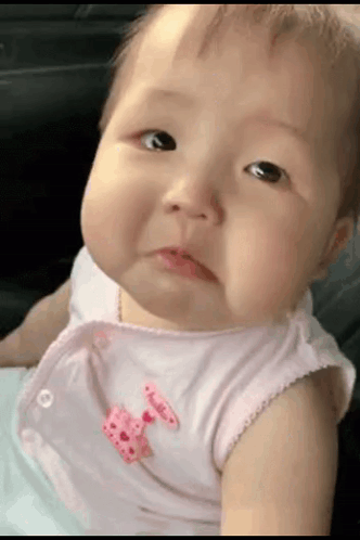 A Baby With A Pink Bow On Her Shirt Is Making A Funny Face GIF