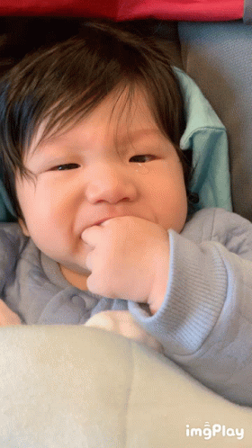 A Baby With A Tear Coming Out Of His Eye Is Sitting In A Stroller With A Blue Sweater On GIF