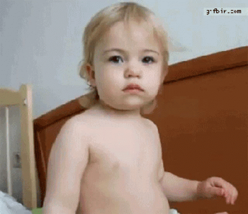 A Baby Without A Shirt Is Standing In Front Of A Bed With The Website Gfbir.com Visible In The Corner GIF