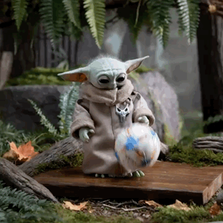 A Baby Yoda Is Holding A Soccer Ball In His Hands . GIF