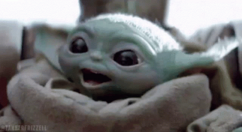 A Baby Yoda Is Sitting In A Blanket And Looking At The Camera . GIF