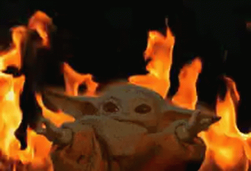 A Baby Yoda Is Standing In Front Of A Fire In A Dark Room . GIF
