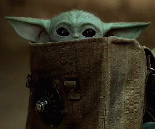 A Baby Yoda Looks Out Of A Brown Bag GIF