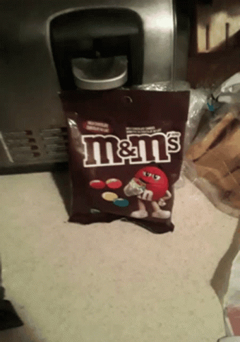 A Bag Of M & M 'S Sits On A Counter In Front Of A Coffee Maker GIF