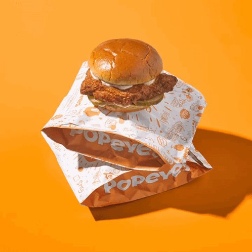 A Bag Of Popeye 'S Chicken Sandwiches On An Orange Background GIF