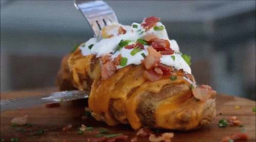 A Baked Potato Covered In Cheese Bacon Sour Cream And Green Onions GIF
