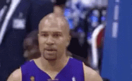 A Bald Basketball Player Wearing A Purple Jersey Is Standing In Front Of A Blue Wall . GIF