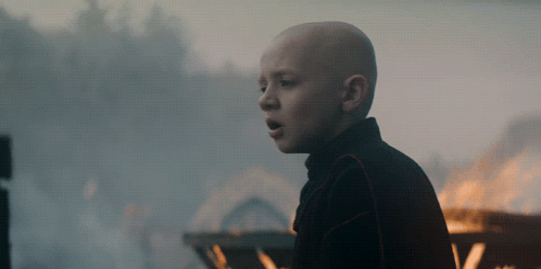 A Bald Boy Stands In Front Of A Fire With His Mouth Open GIF