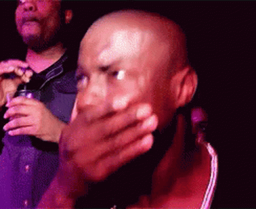 A Bald Man Covering His Mouth With His Hand While Another Man Holds A Microphone GIF