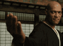 A Bald Man In A Black Robe Is Waving His Hand In Front Of A Window GIF