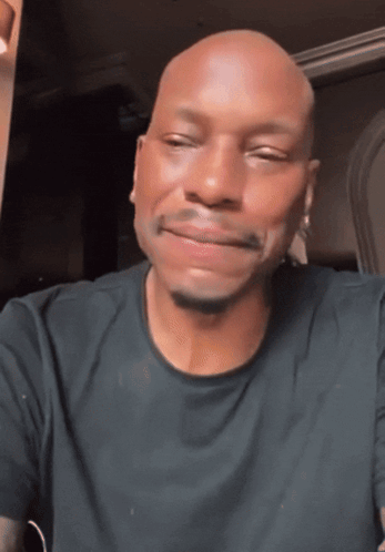 A Bald Man In A Black Shirt Is Smiling GIF
