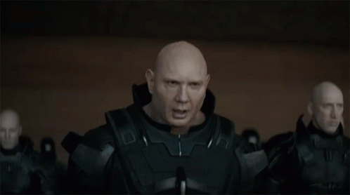 A Bald Man In A Black Suit Is Standing In Front Of A Group Of Bald Men GIF