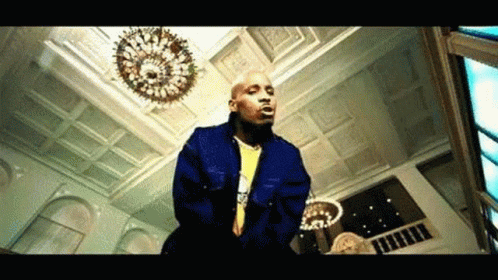 A Bald Man In A Blue Jacket Is Standing In A Room With A Chandelier . GIF