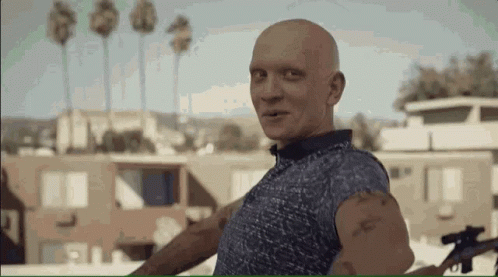 a bald man in a blue shirt is holding a gun and smiling